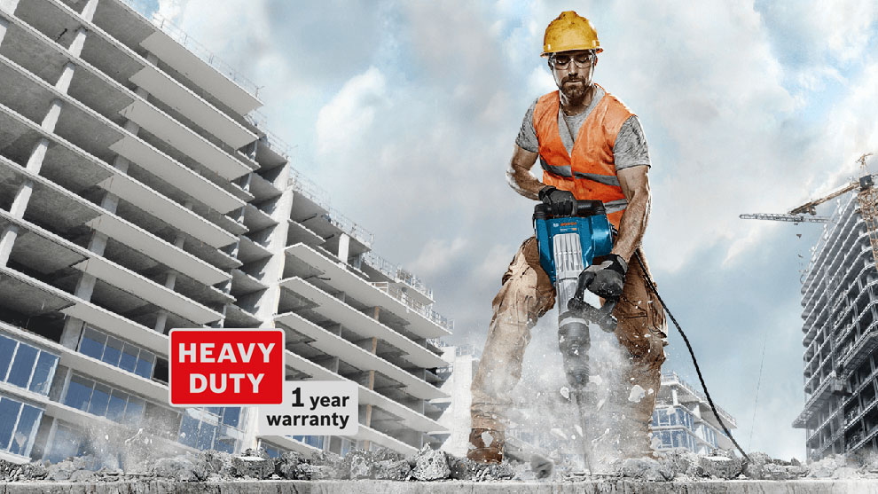 A man in a hard hat uses a Bosch demolition hammer on a construction site.