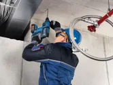 A person wearing safety equipment drills into a concrete ceiling using a rotary hammer.