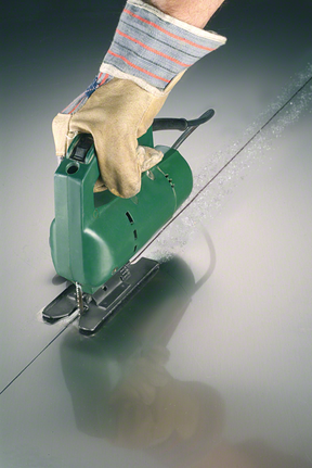 Person wearing safety equipment uses a jigsaw to cut a straight line in metal.