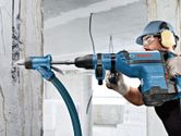 A person wearing safety equipment drills into concrete with a rotary hammer and dust extraction.