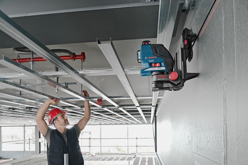 A person wearing safety equipment aligns ceiling frames using a laser leveling tool on a universal mount.