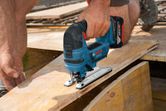A person cuts plywood on a construction site using a cordless jigsaw.