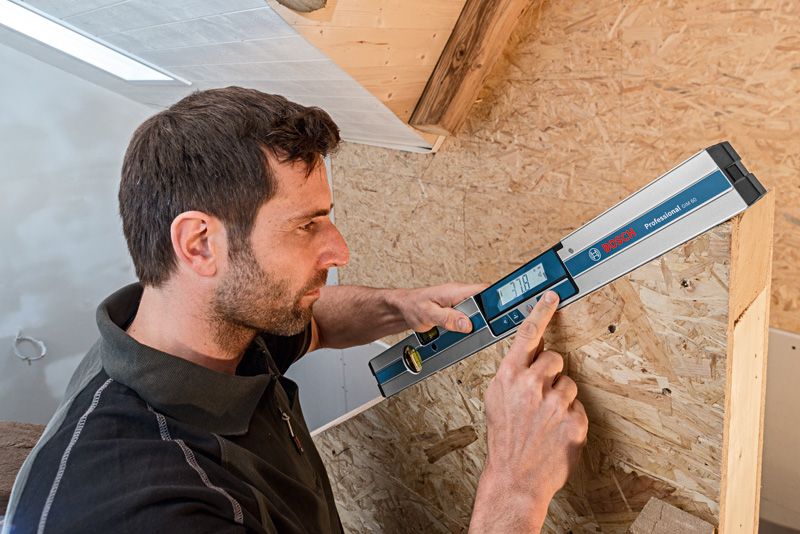 GIM 60 A person uses a digital inclinometer to measure the angle of a wooden structure.