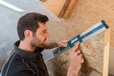 A person uses a digital inclinometer to measure the angle of a wooden structure.