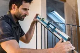 A person measures the angle of a railing using a digital inclinometer.