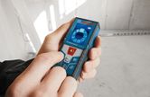 Person operating a digital laser measure in an unfinished room.