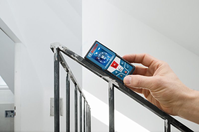 A person measures the angle of a stair railing with a laser measure.