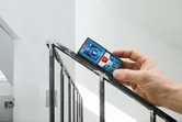Person using a laser measure on a metal stair railing to check distance or angle.