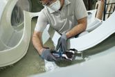 A person wearing safety equipment cuts fiberglass with a cordless multi-tool.