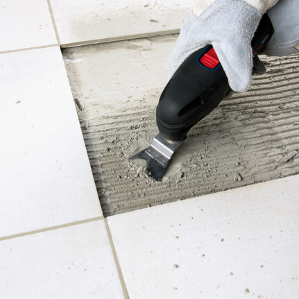 3-piece basic tile set Worker wearing safety equipment uses a multi-tool to remove adhesive between floor tiles.