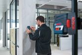 Person marking a concrete pillar using a laser receiver in a modern office space.