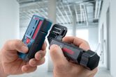 A person assembles a laser measure and bracket in a building under construction.