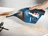 Person using a cordless vacuum cleaner to remove sawdust from a wooden surface.