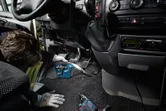 A person wearing safety equipment cleans a car floor with a cordless vacuum cleaner.