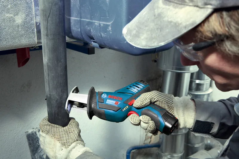 GSA 12V-Li A person wearing safety equipment uses a cordless reciprocating saw to cut a pipe.