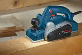 Electric planer smoothing a wooden plank on a workbench.