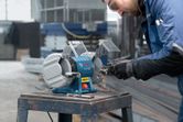 A person wearing safety equipment sharpens metal using a double-wheeled bench grinder.