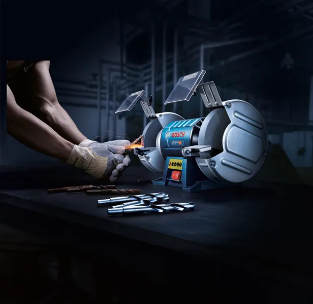 GBG 60-20 A person wearing safety equipment sharpens a drill bit with a double-wheeled bench grinder.