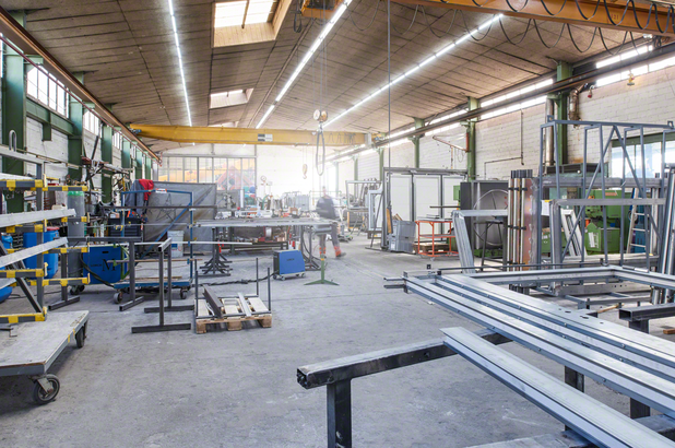 Worker wearing safety equipment moves through a metal fabrication workshop.