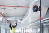 A person wearing safety equipment aligns ceiling frames using a laser leveling tool.