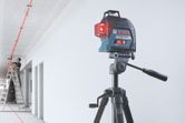 Laser leveling tool projects red lines across a ceiling as a person on a ladder works.