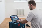 Person analyzing thermal camera data on a laptop in a room with a radiator.