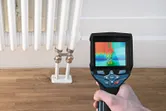 A person uses a thermo camera to inspect heat distribution on a radiator.