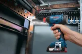Person driving a screw into a metal frame inside an electrical panel.