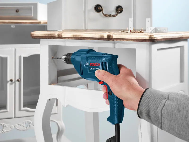 GBM 350 A person drills a hole in a wooden drawer with a blue electric drill.