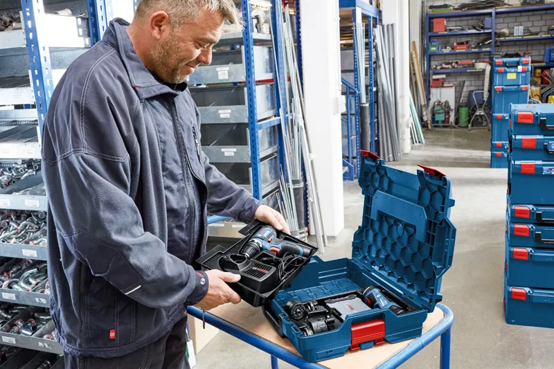 A person in a workshop unpacks a cordless tool set from a hard plastic case.