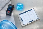 Laser measure on blueprints beside a digital tablet displaying building plans.