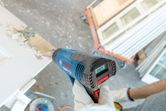A person wearing safety equipment uses a heat gun to strip paint from a door.