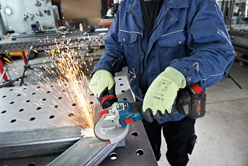 A person wearing safety equipment uses an angle grinder to cut metal, creating sparks.