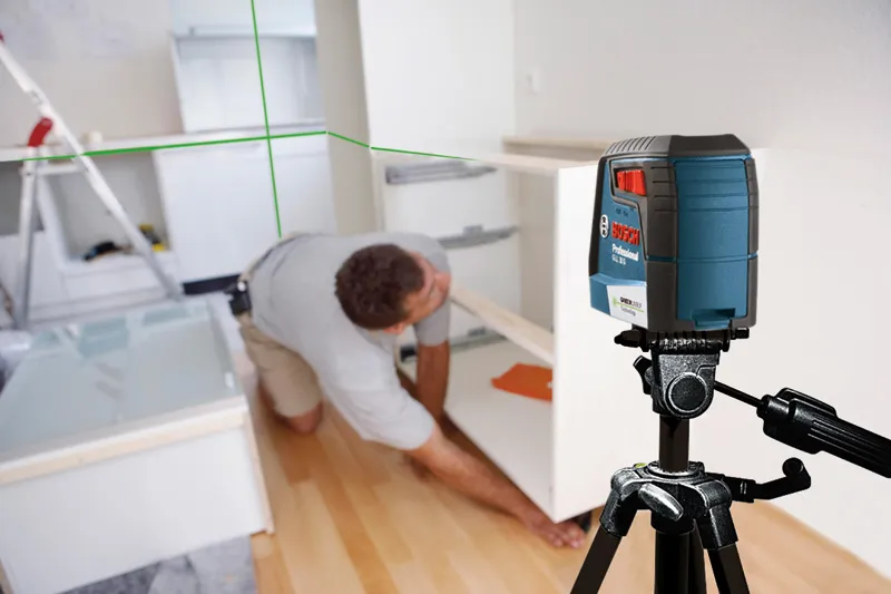 A person installs a cabinet in a kitchen using a laser leveling tool on a tripod.