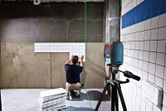 Person installs wall tiles using a laser leveling tool to align rows.