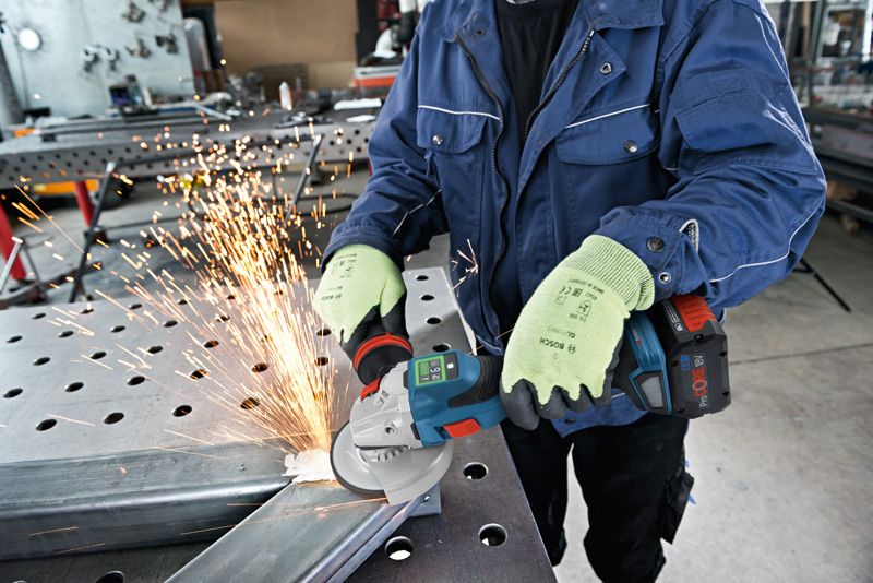 A person wearing safety equipment grinds metal with a power tool, creating sparks.