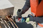 A person wearing safety equipment grinds rebar extending from a concrete block.