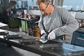 A person wearing safety equipment grinds metal beams with an angle grinder, producing sparks.