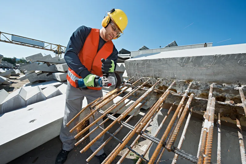 GWS 18V-10 A person wearing safety equipment cuts rebar with a power tool at a construction site.