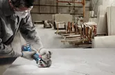 A person wearing safety equipment cuts a slab with a cordless angle grinder in a workshop.