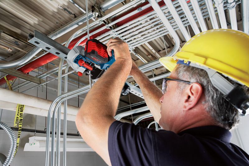 GCB 18V-63 A person wearing safety equipment uses a cordless band saw to cut metal conduit overhead.