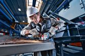 A person wearing safety equipment grinds metal with a cordless angle grinder, producing sparks.