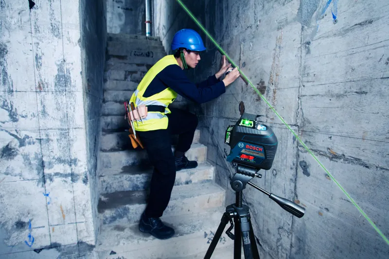 A person wearing safety equipment marks a wall guided by a laser leveling tool.