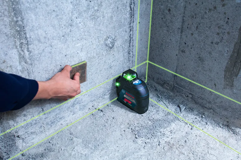 Person using a sanding block on a concrete wall, next to an active laser leveling tool.