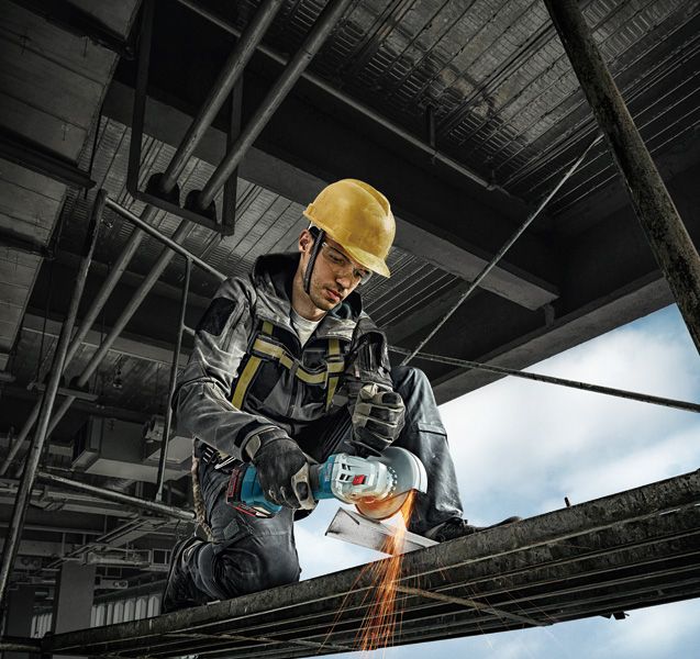 GWS 180-LI A person wearing safety equipment uses an angle grinder to cut metal scaffolding.