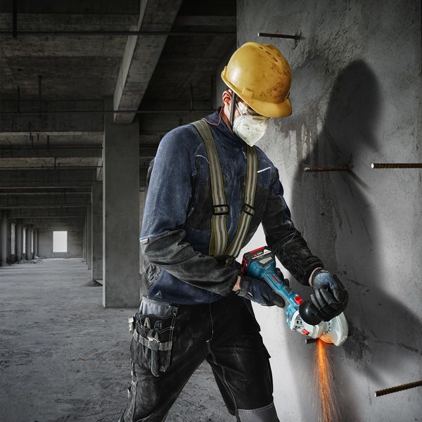 GWS 180-LI A person wearing safety equipment cuts concrete with an angle grinder.