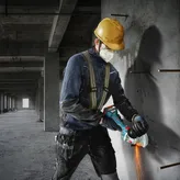 A person wearing safety equipment cuts concrete with an angle grinder.