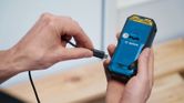 A person connects a charging cable to the back of a handheld power tool.