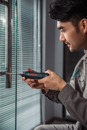 Person fastens a screw on a glass door handle with a cordless screwdriver.