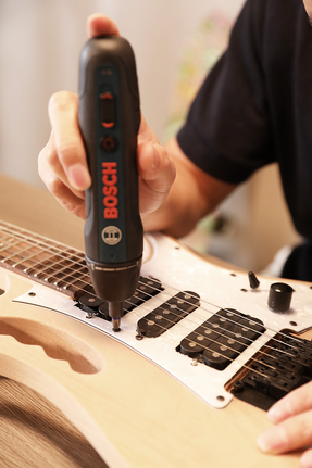 Person using a power screwdriver to assemble an electric guitar.